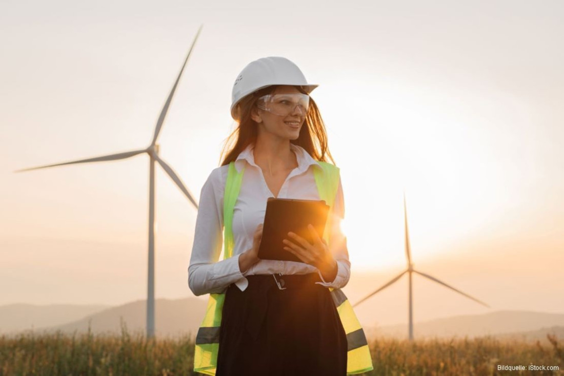 Frau mit Helm und Tablet im Hindergrund zwei Windräder